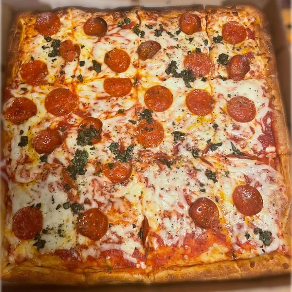 A square pepperoni pizza with melted cheese, tomato sauce, and basil, cut into squares.