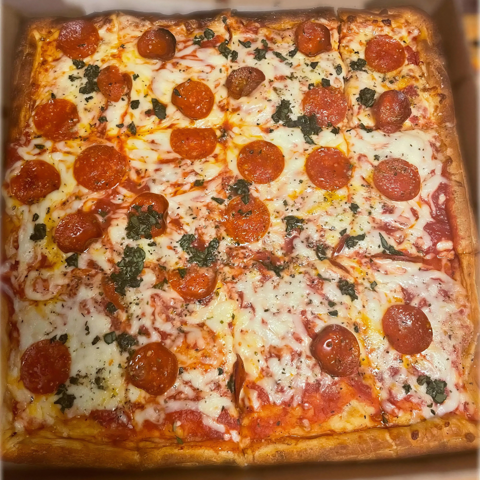 A square pepperoni pizza with melted cheese, tomato sauce, and basil, cut into squares.