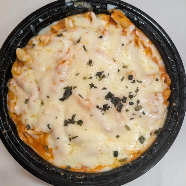 Penne pasta with melted cheese and herbs in a black bowl, seen from directly above.