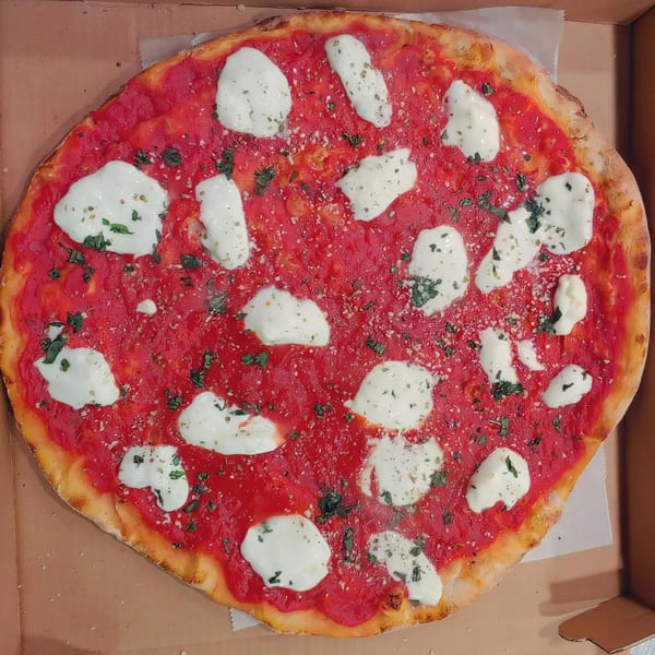 A whole Margherita pizza with fresh mozzarella, red sauce, and basil in a cardboard box.