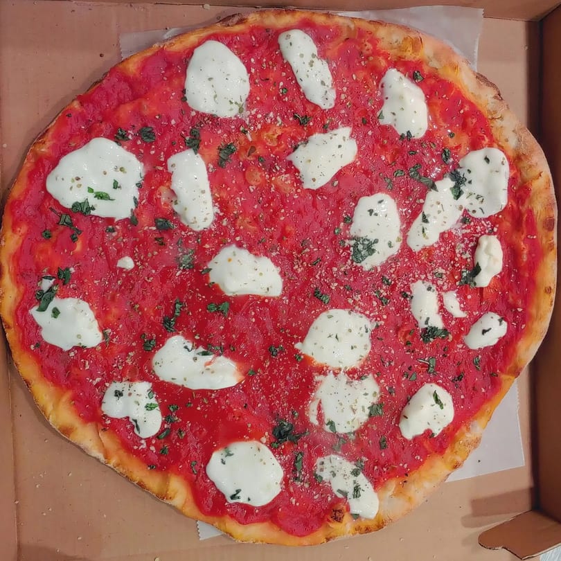 A whole Margherita pizza with fresh mozzarella, red sauce, and basil in a cardboard box.